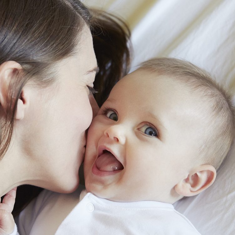 Portrait of cute baby girl being kissed by mother on bed